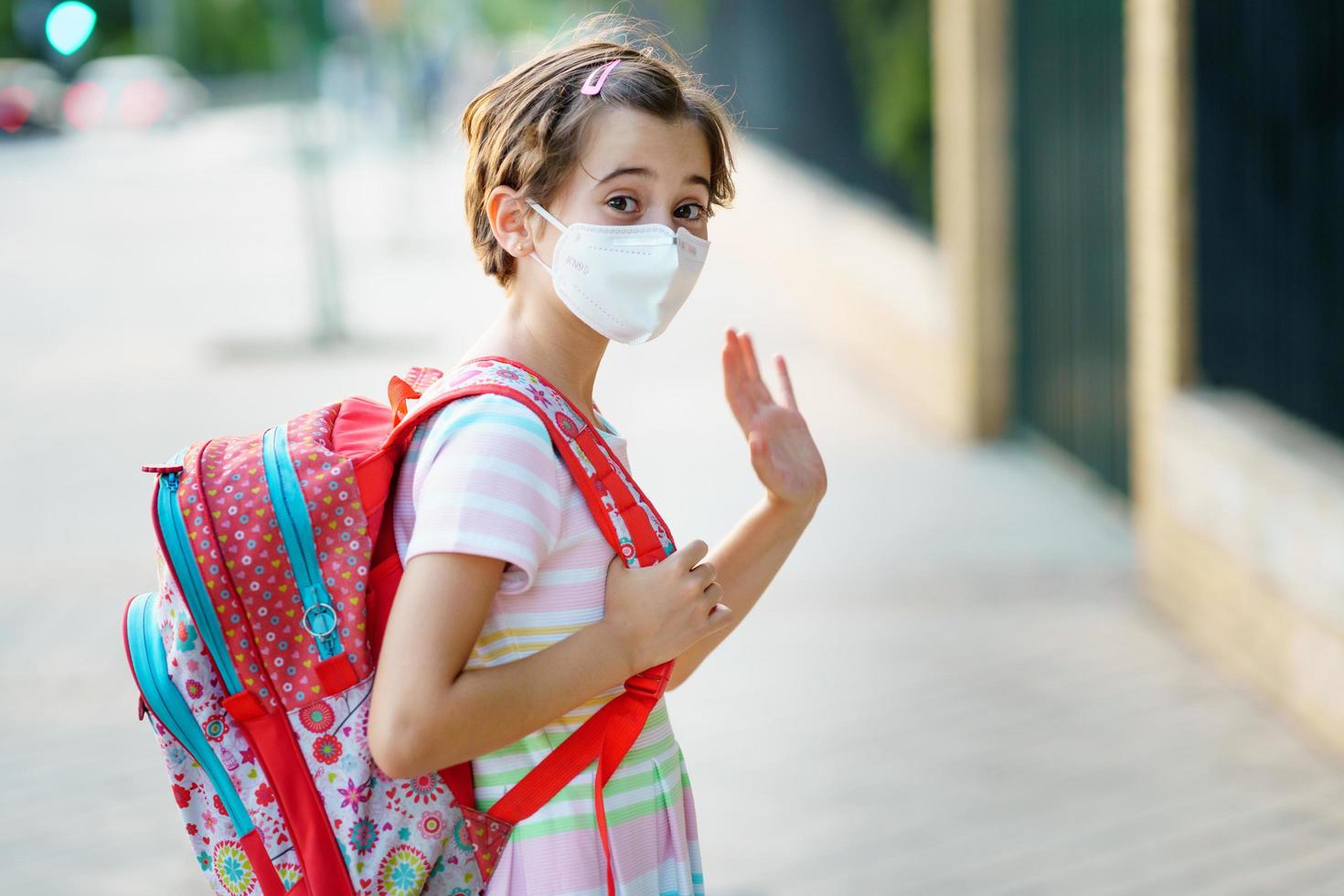 bambina di nove anni torna a scuola indossando una maschera e una cartella. foto