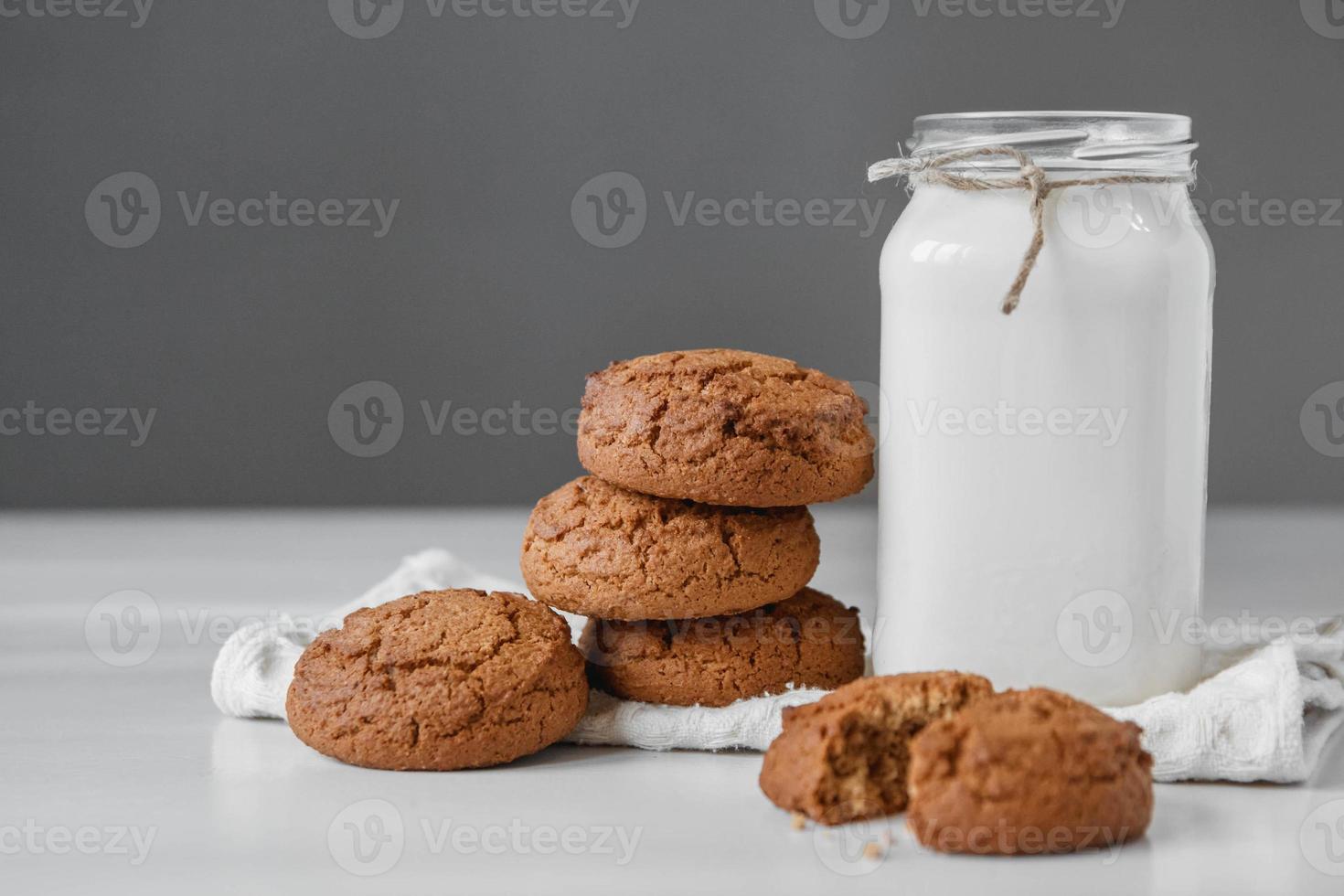 latte in un barattolo di vetro e biscotti di farina d'avena vicino al tovagliolo su sfondo bianco della tavola foto