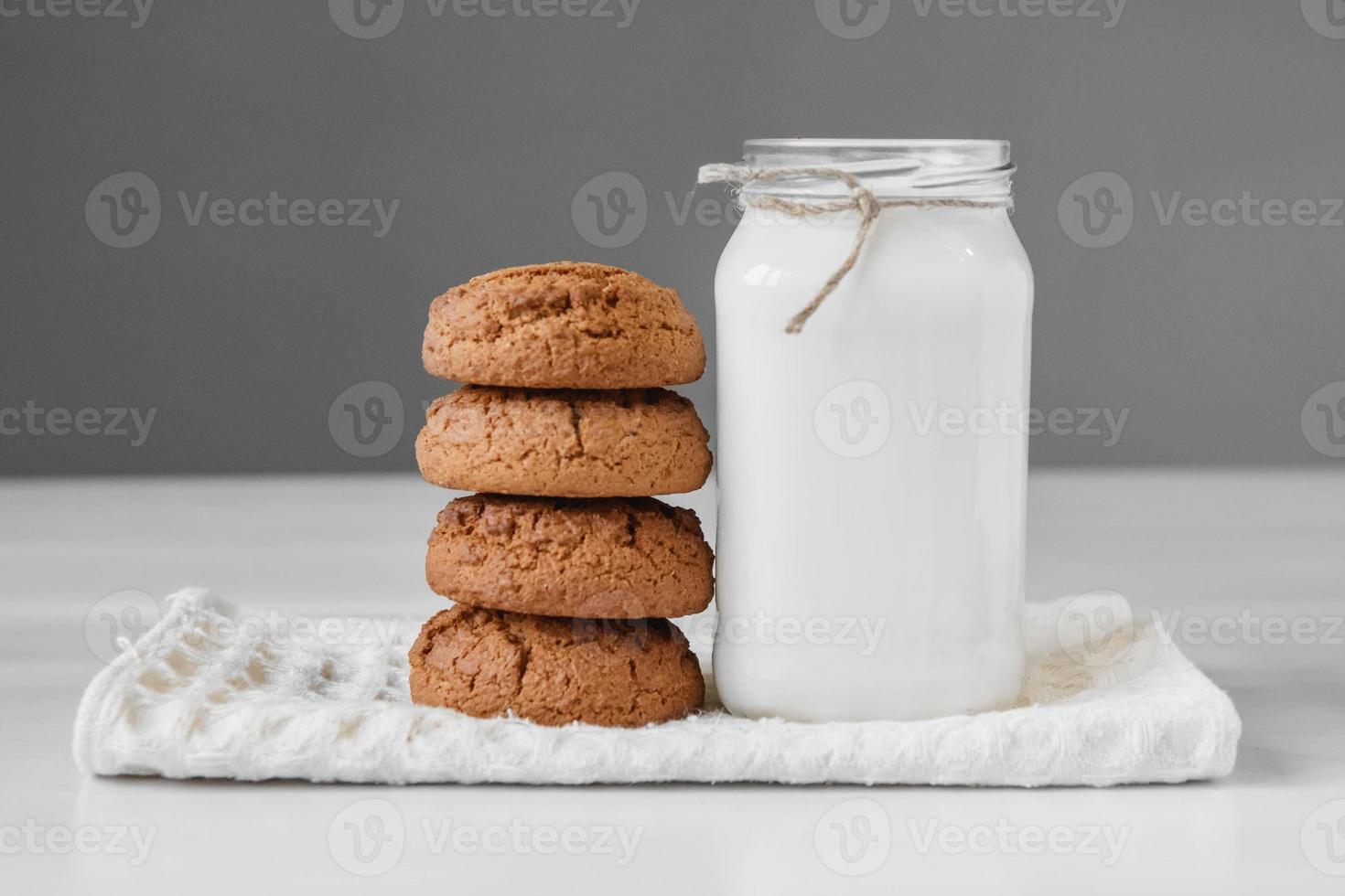 latte in barattolo di vetro e biscotti di farina d'avena vicino al tovagliolo sul tavolo bianco foto