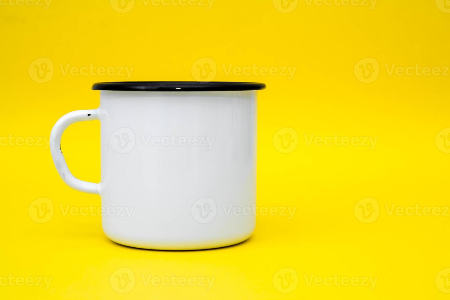 tazza in metallo smaltato bianco con linea nera sul bordo su sfondo giallo foto