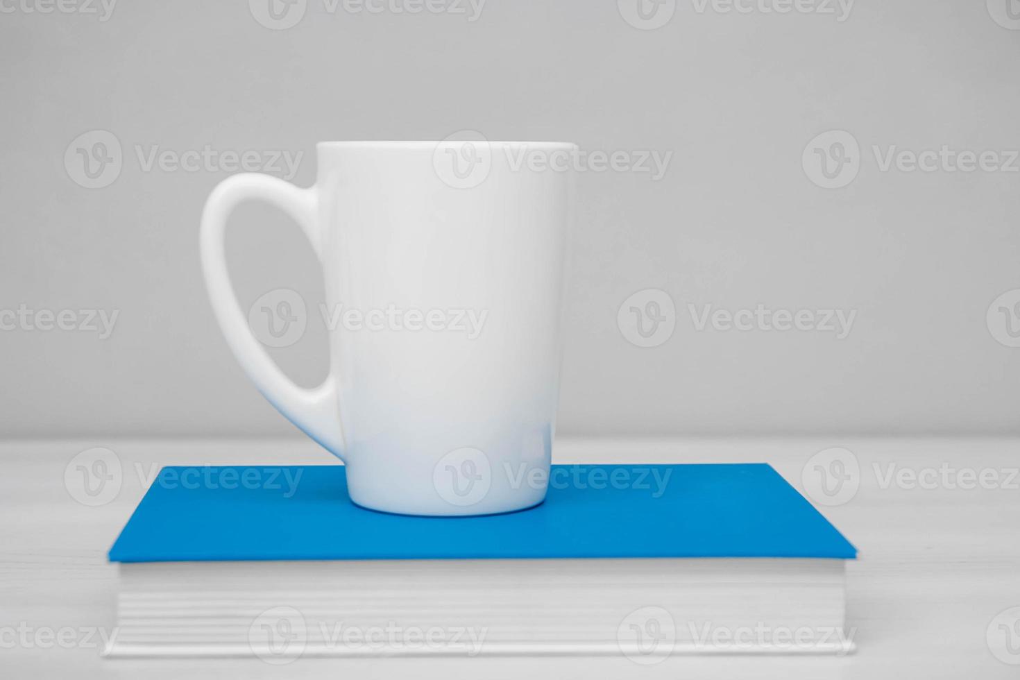 tazza in ceramica bianca e libro sul tavolo bianco foto