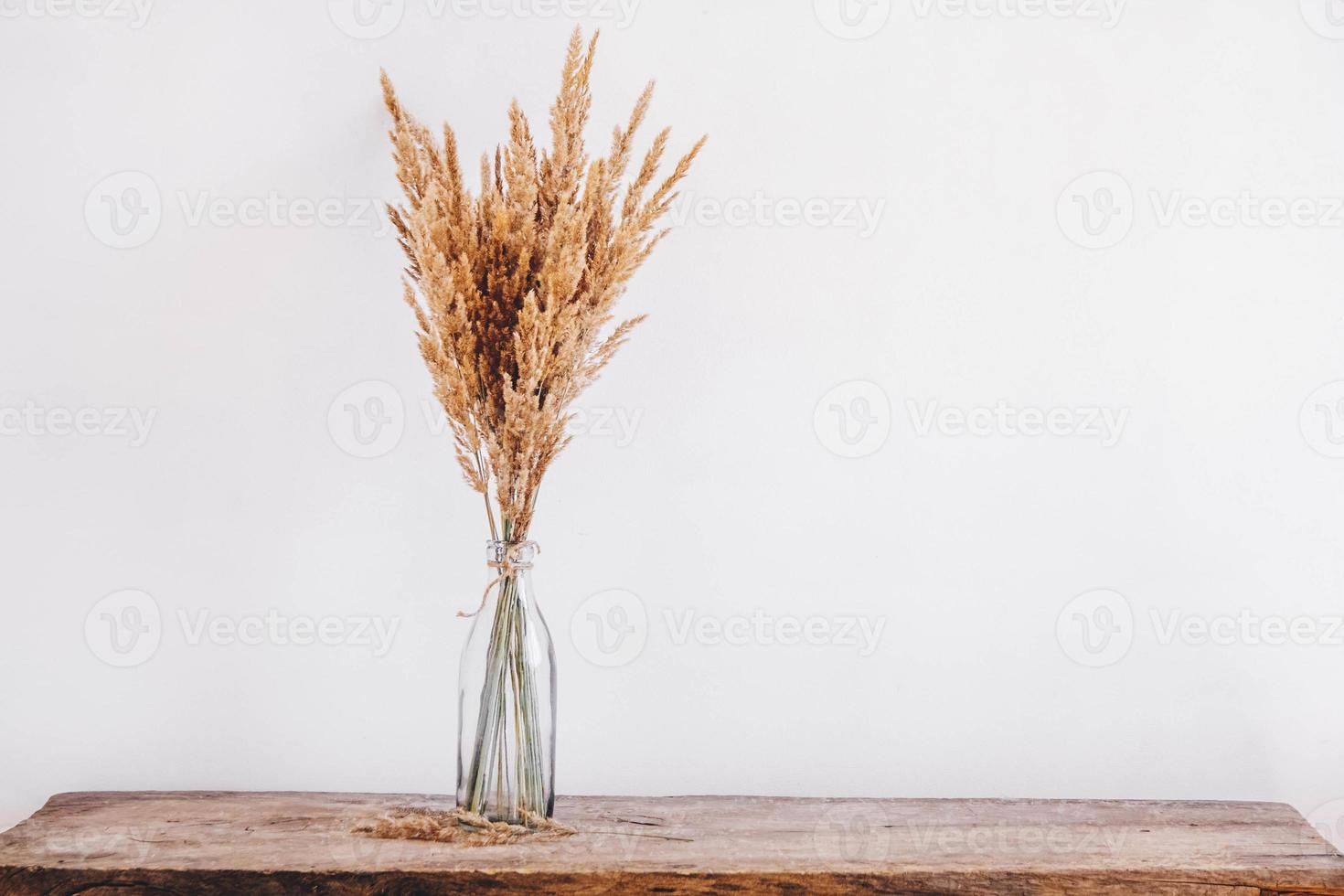 natura morta di un mazzo di fiori secchi in una bottiglia di vetro su un tavolo di legno foto