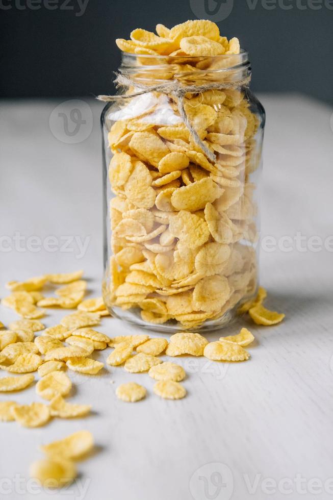 fiocchi di mais in un barattolo di vetro su superficie di legno bianco foto
