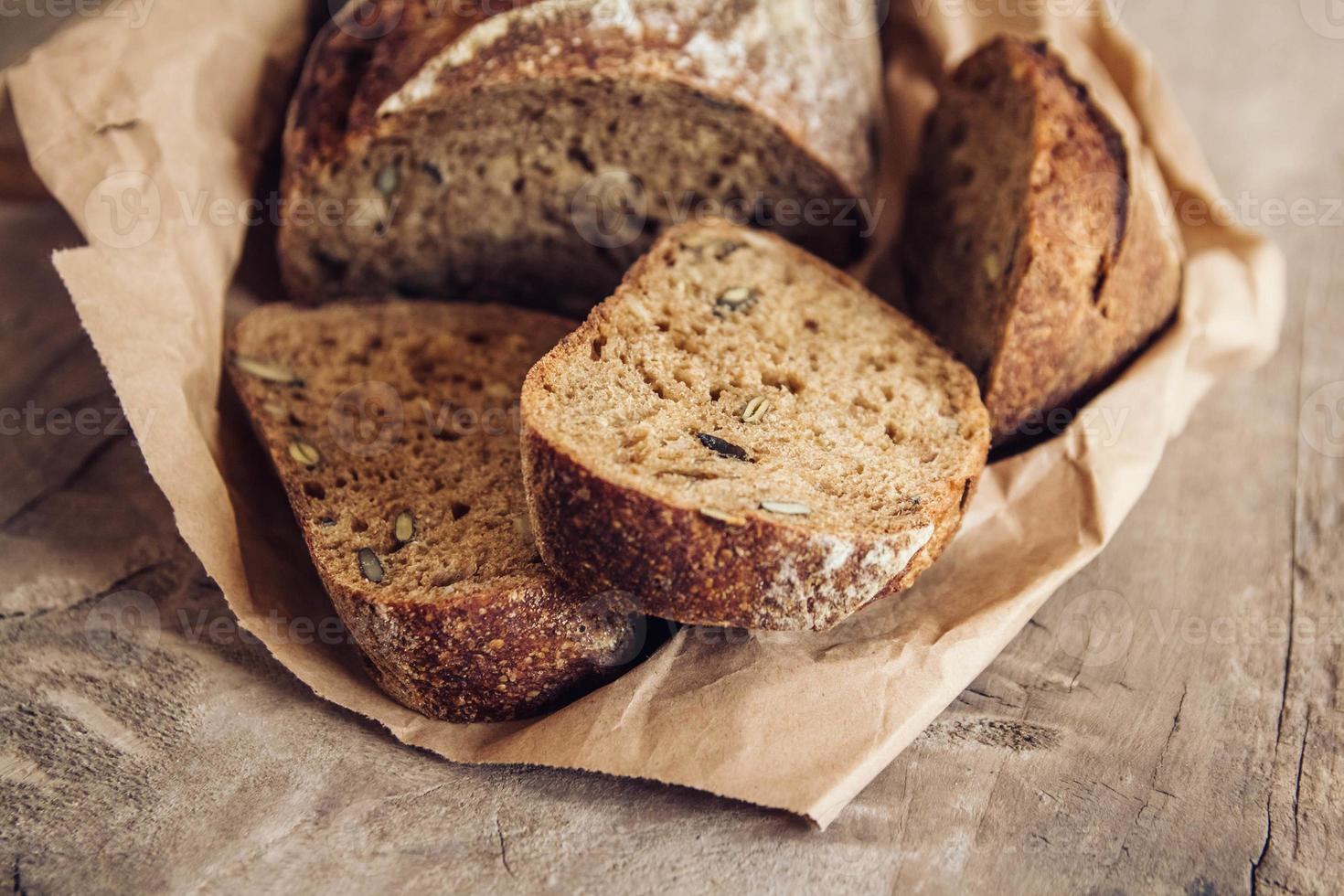 il pane fresco marrone con i semi viene tagliato a pezzi su uno sfondo di legno vecchio foto