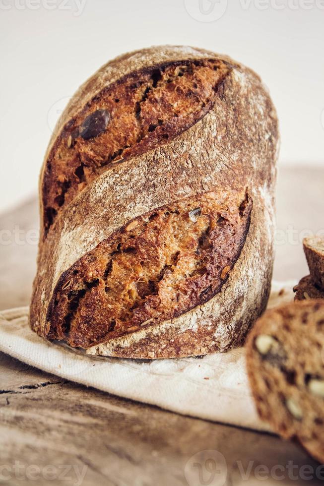 il pane fresco marrone con i semi viene tagliato a pezzi su uno sfondo di legno vecchio foto