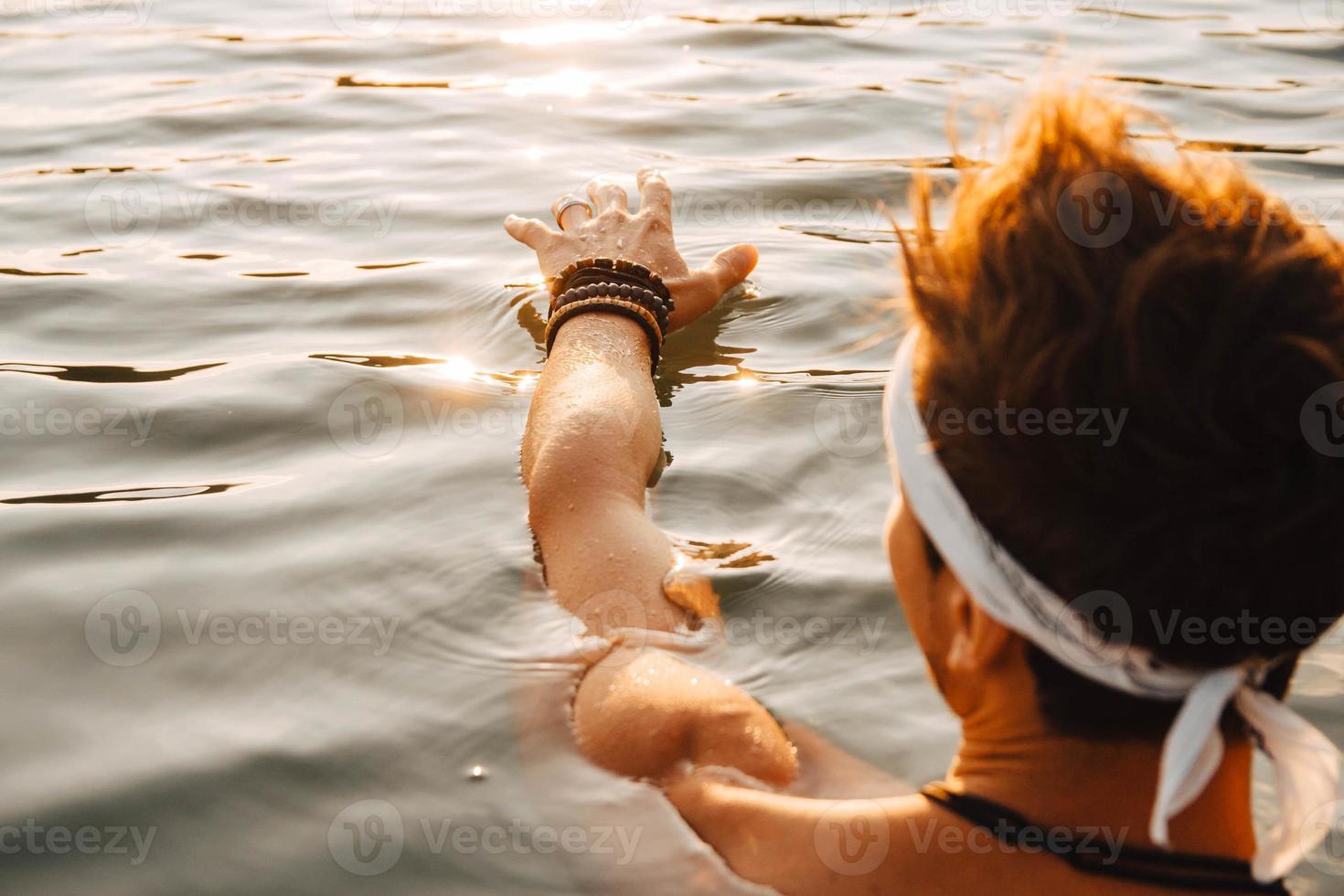 l'uomo tocca l'acqua con la mano al tramonto foto