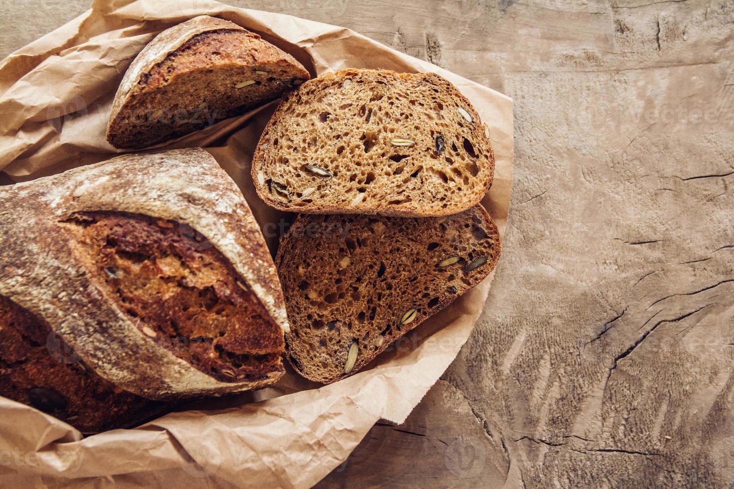 il pane fresco marrone con i semi viene tagliato a pezzi su uno sfondo di legno vecchio foto