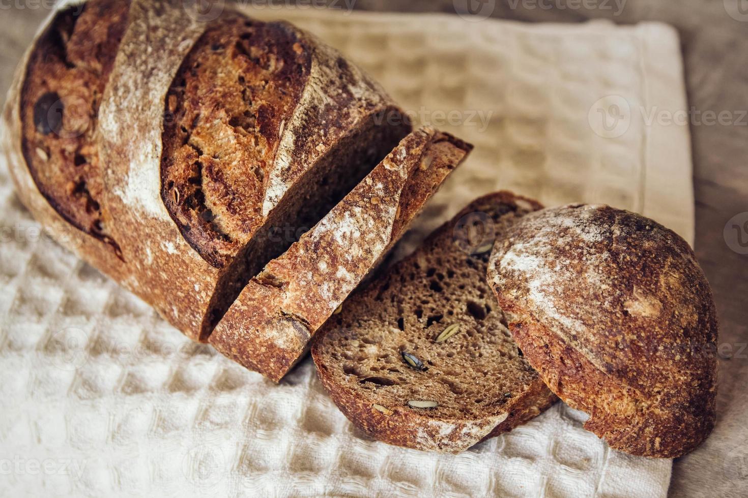 il pane fresco marrone con i semi viene tagliato a pezzi su uno sfondo di legno vecchio foto