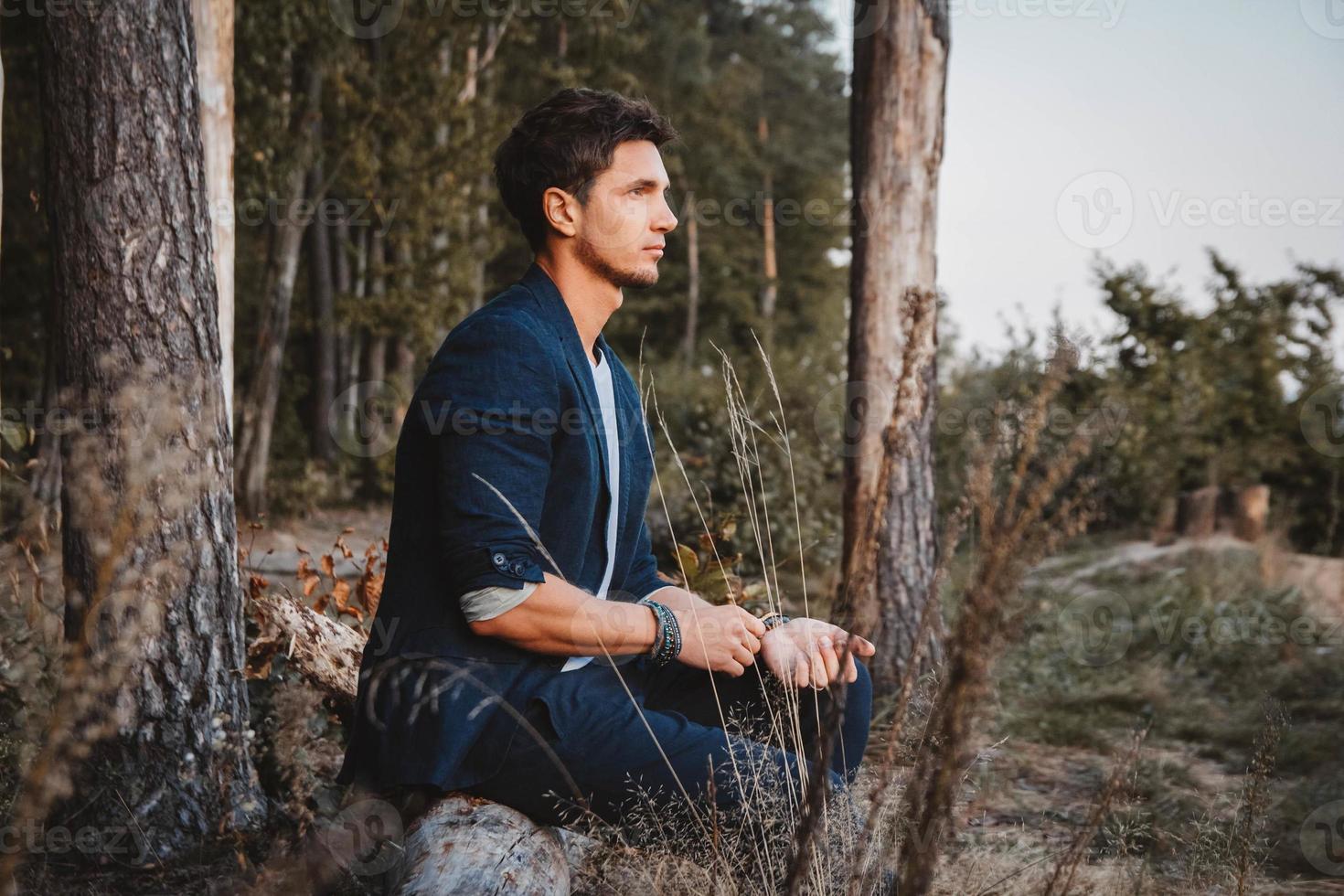 l'uomo in posa all'aperto nella foresta si siede su un tronco indossando una giacca a quadri foto