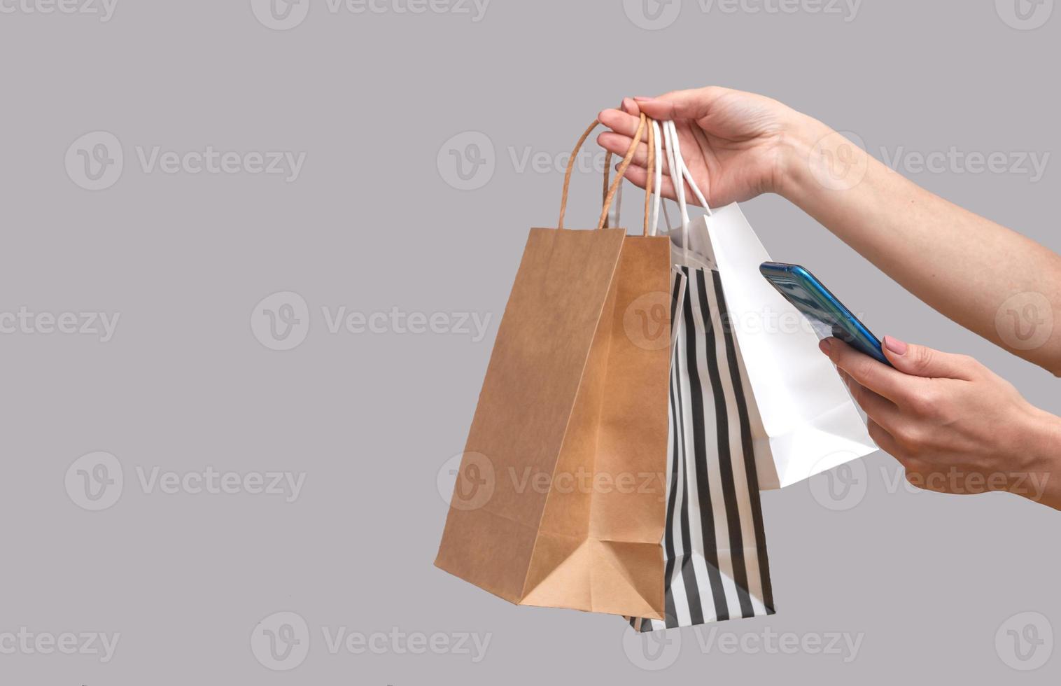 donna che acquista online da un telefono cellulare. mani femminili con pacchetti isolati su sfondo grigio, spazio copia foto