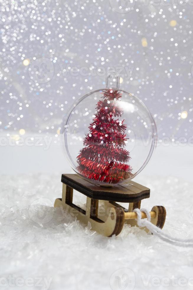 sulla neve - una slitta con una palla di natale all'interno di un albero di natale su uno sfondo di luci bokeh ravvicinate. foto verticale