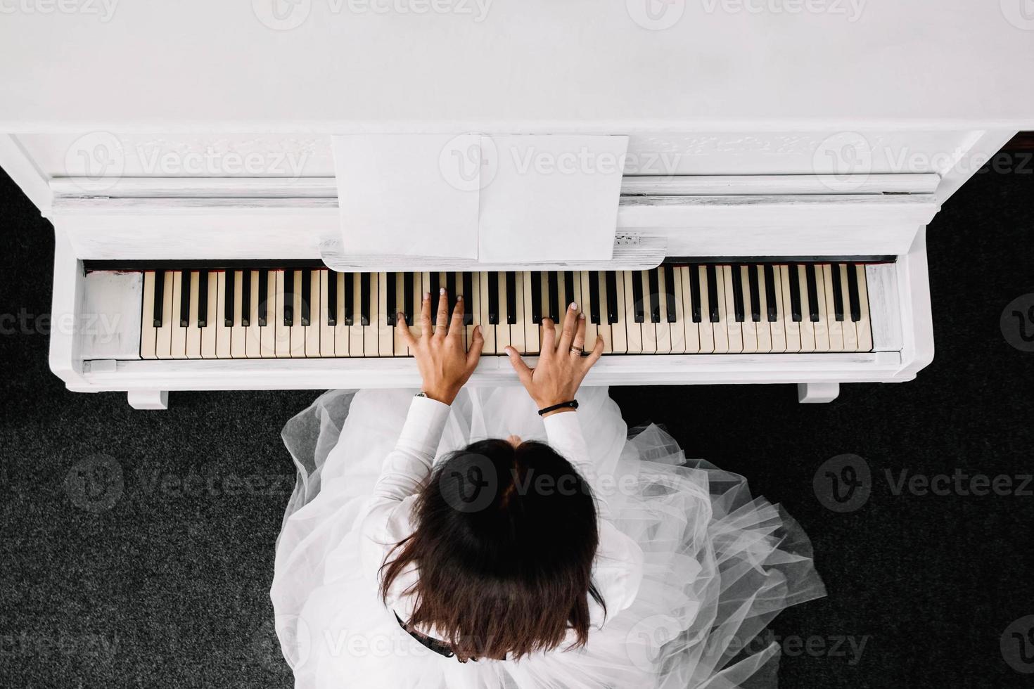 bella donna vestita in abito bianco, suonare il pianoforte bianco. vista dall'alto foto