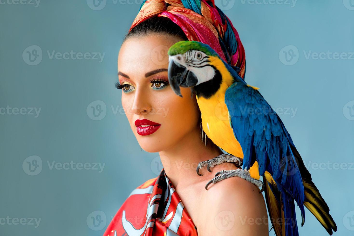 ritratto di giovane donna attraente in stile africano con ara pappagallo sulla mano su sfondo colorato foto