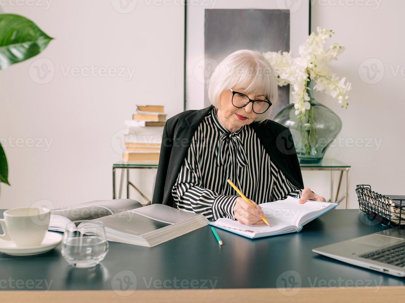 senior bei capelli grigi donna acqua potabile durante il lavoro in ufficio. lavoro, anziani, bilancio idrico, trovare una soluzione, sperimentare il concetto foto