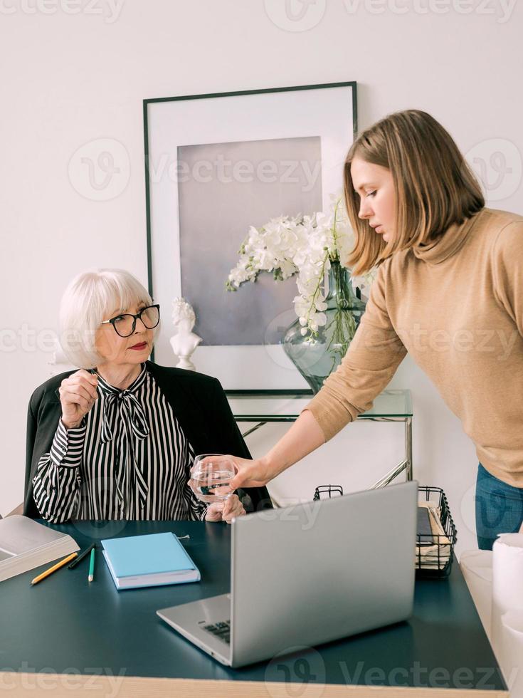 il giovane assistente portò un bicchiere d'acqua al capo in carica. business, comunicazione, lavoro, età, collaborazione, concetto di mentoring foto