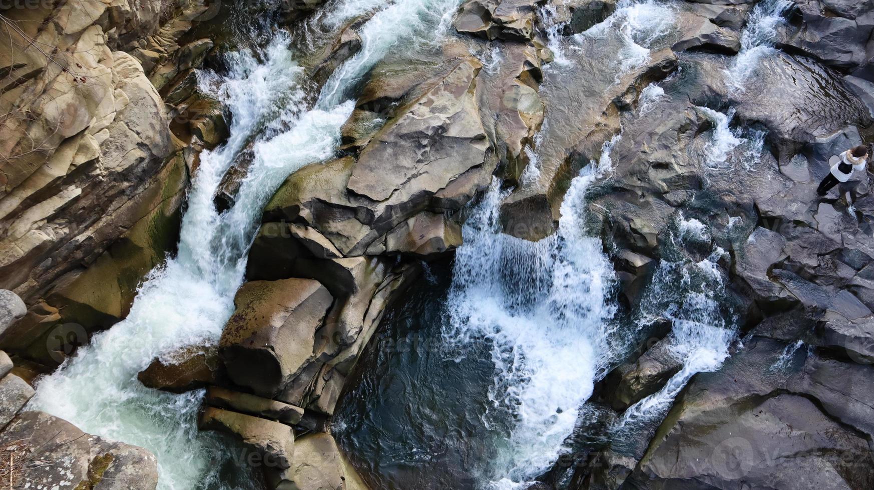 vista dall'alto verso il basso della cascata. vista dall'alto del torrente, l'acqua scorre sulle pietre. cascata di montagna rocciosa. paesaggio aereo montagna cascata rocciosa fiume ruscello sfondo scenico naturale immagine foto