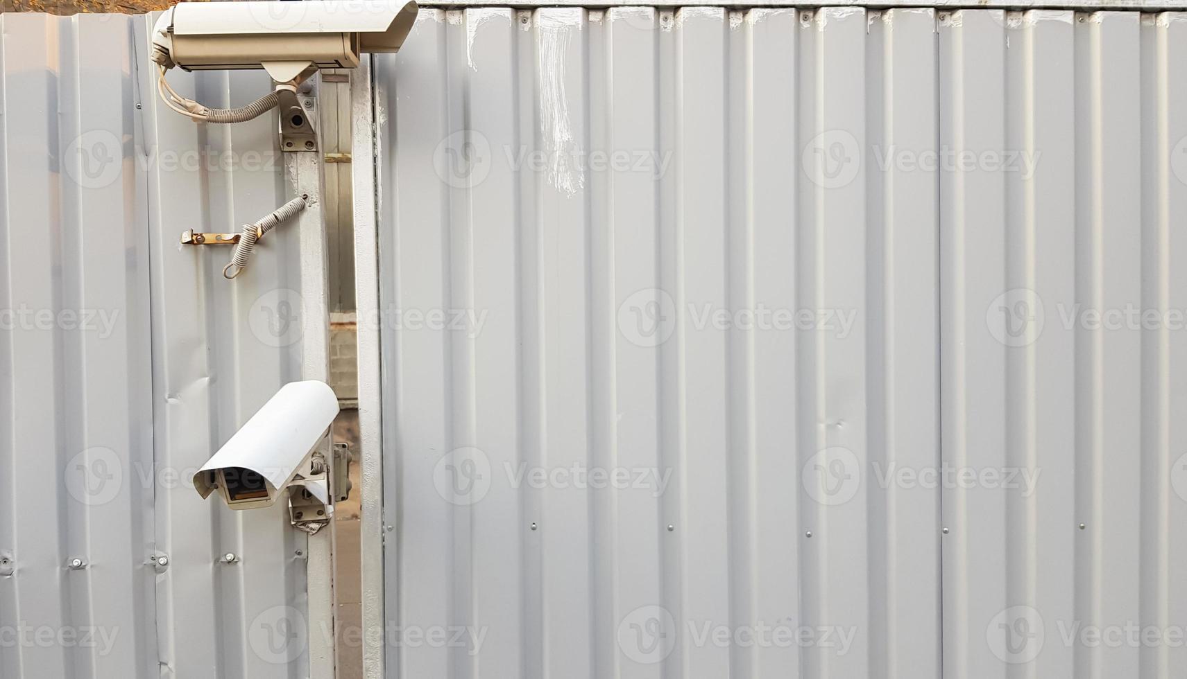 telecamera di sorveglianza in cima a una recinzione metallica ondulata grigia foto