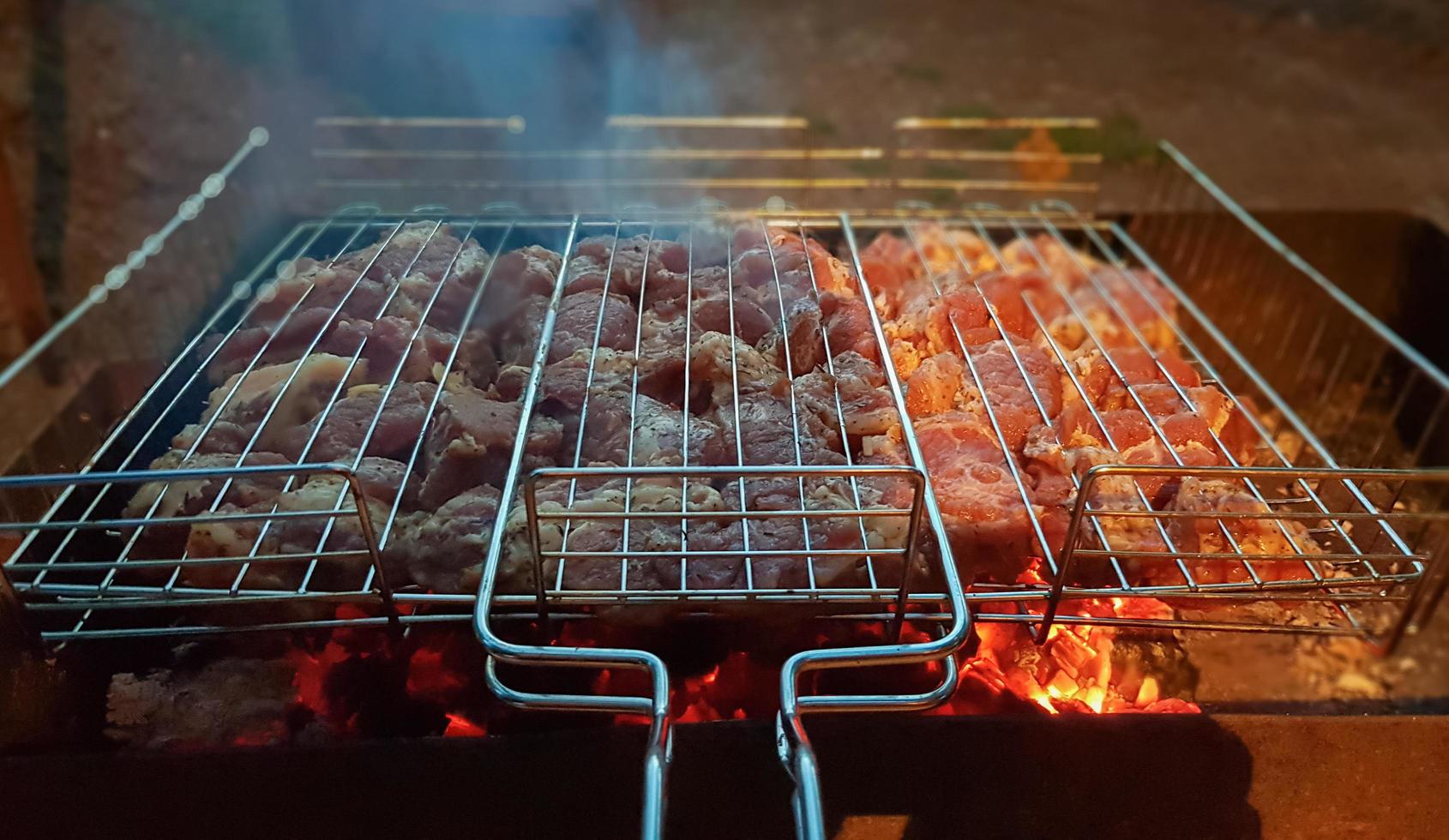 il processo di cottura dello shish kebab alla griglia. carne succosa e profumata languisce nel fuoco e nel fumo. concetto di picnic in campagna di notte. piatto da picnic appetitoso e nutriente all'aria aperta. foto