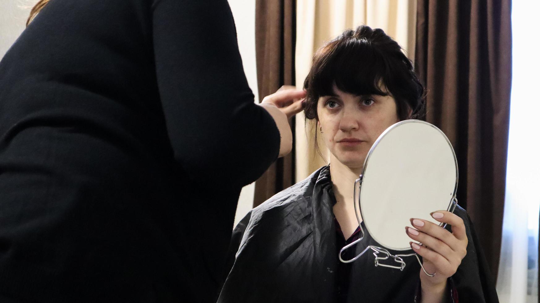 primo piano del maestro parrucchiere che fa acconciatura riccia e trucco per una bella donna con i capelli scuri a casa. acconciatura da sposa per la sposa. foto