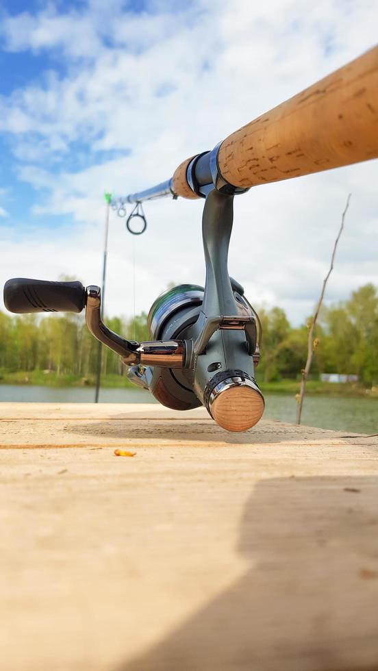 canna da pesca alla carpa isolata sul lago e ponte di legno. alimentatore di carpe bobina di filatura da vicino. pescare carpe sul lago. attrezzatura del pescatore. fotografia verticale. foto