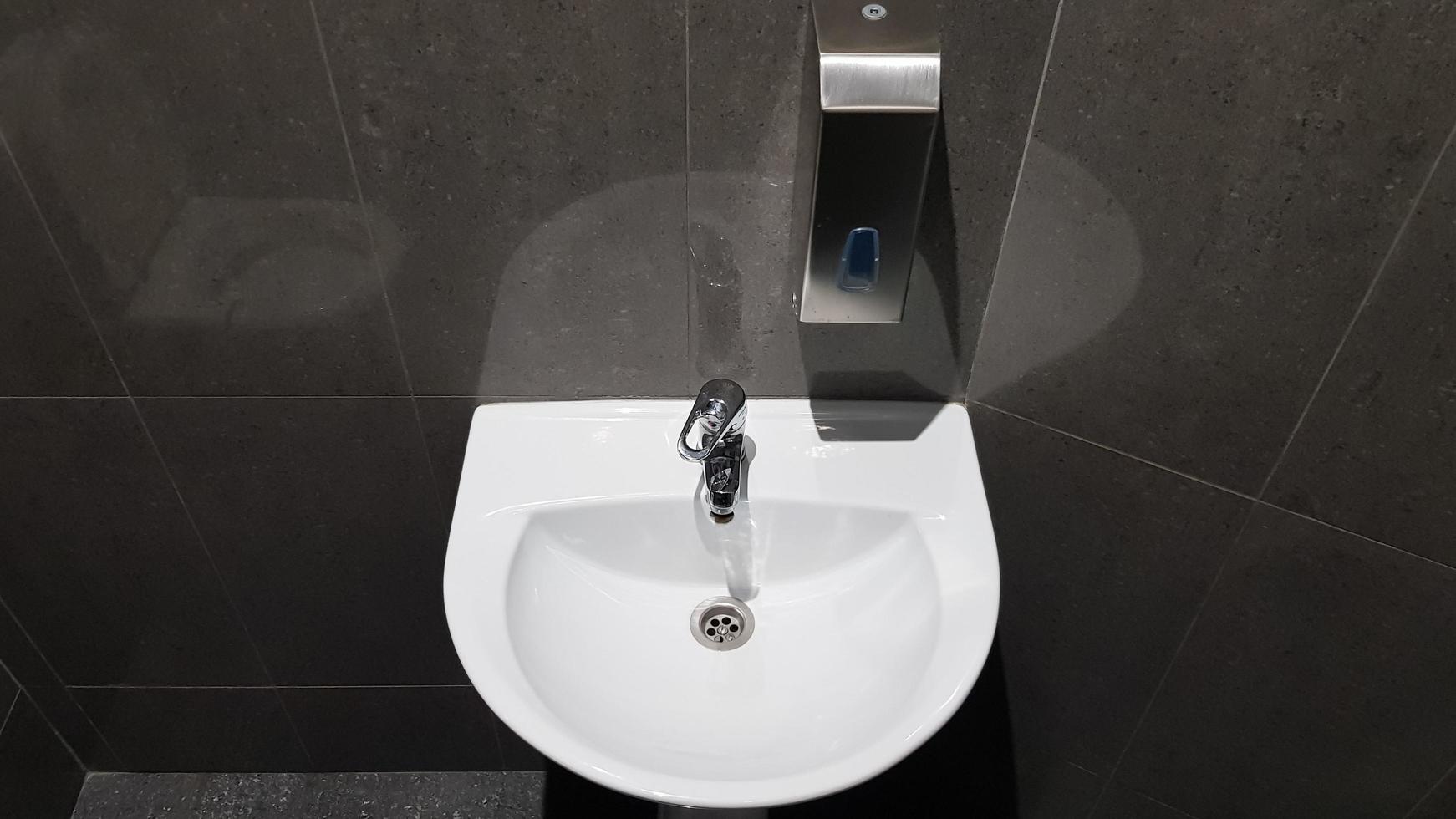 lavabo in ceramica bianca con rubinetto cromato nella toilette con piastrelle grigie foto