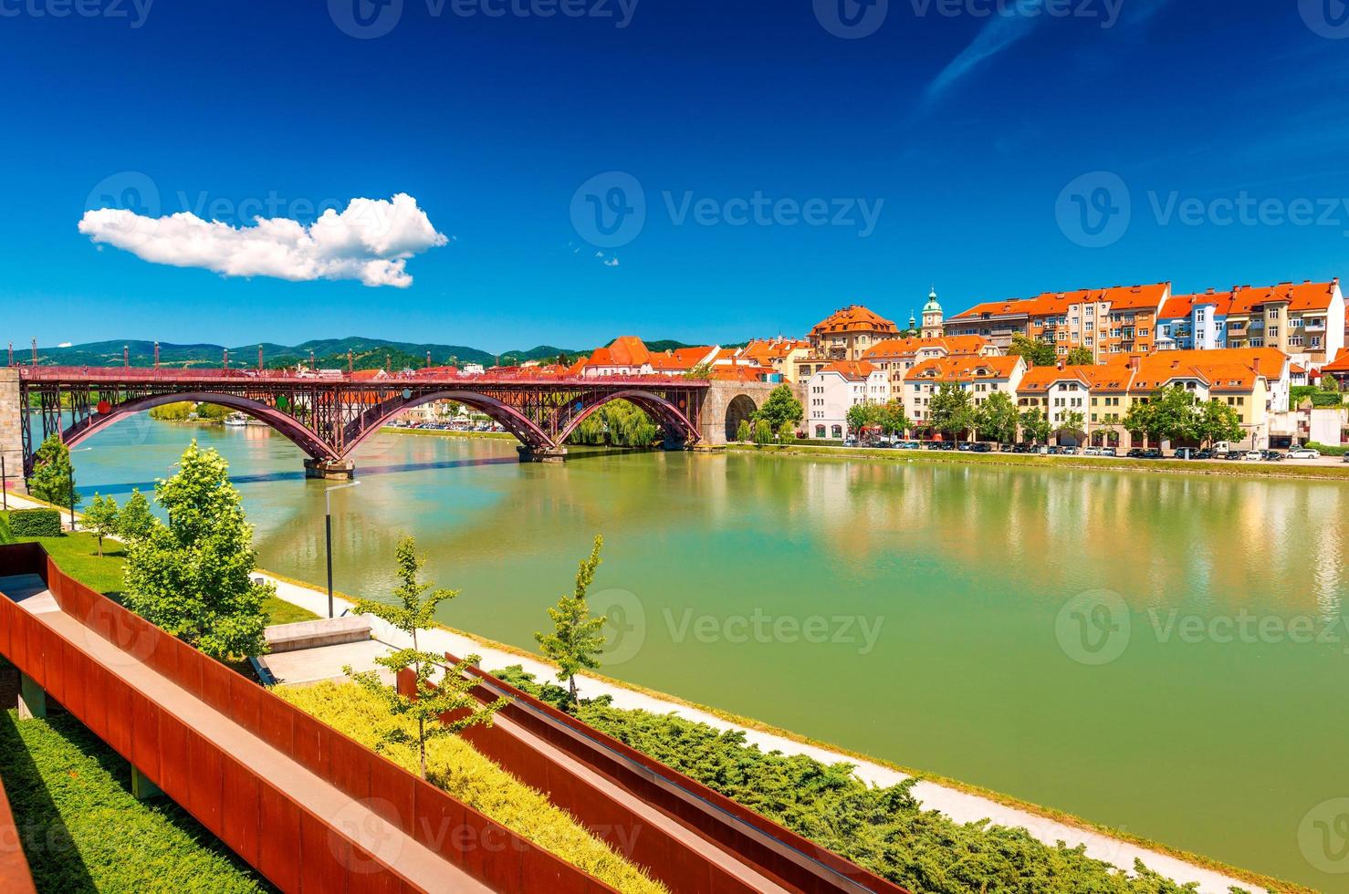 il bellissimo paesaggio urbano di maribor con il vecchio ponte sul fiume drava, l'argine e i vecchi edifici con tetti di tegole arancioni foto