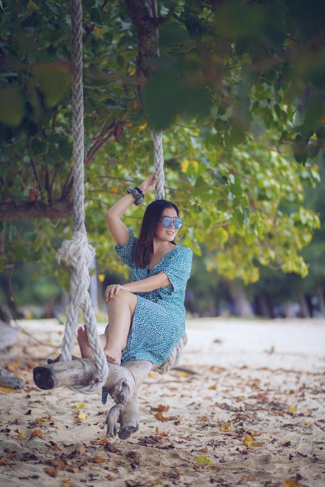 bella donna che si rilassa sull'altalena naturale della spiaggia con la faccia sorridente foto