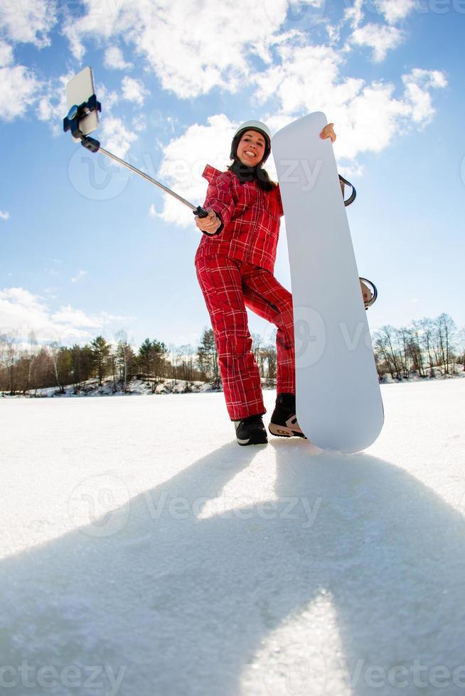 donna con lo snowboard che usa lo smartphone su un bastone per fare selfie foto