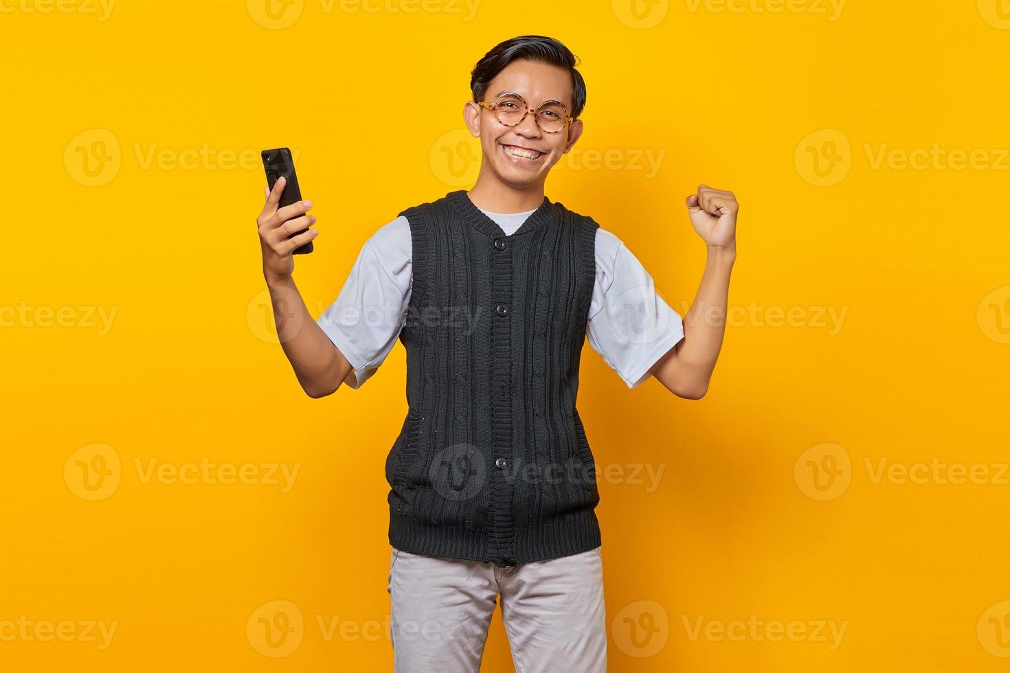 ritratto di un bell'uomo asiatico allegro che tiene in mano lo smartphone e si rallegra celebrando la fortuna foto