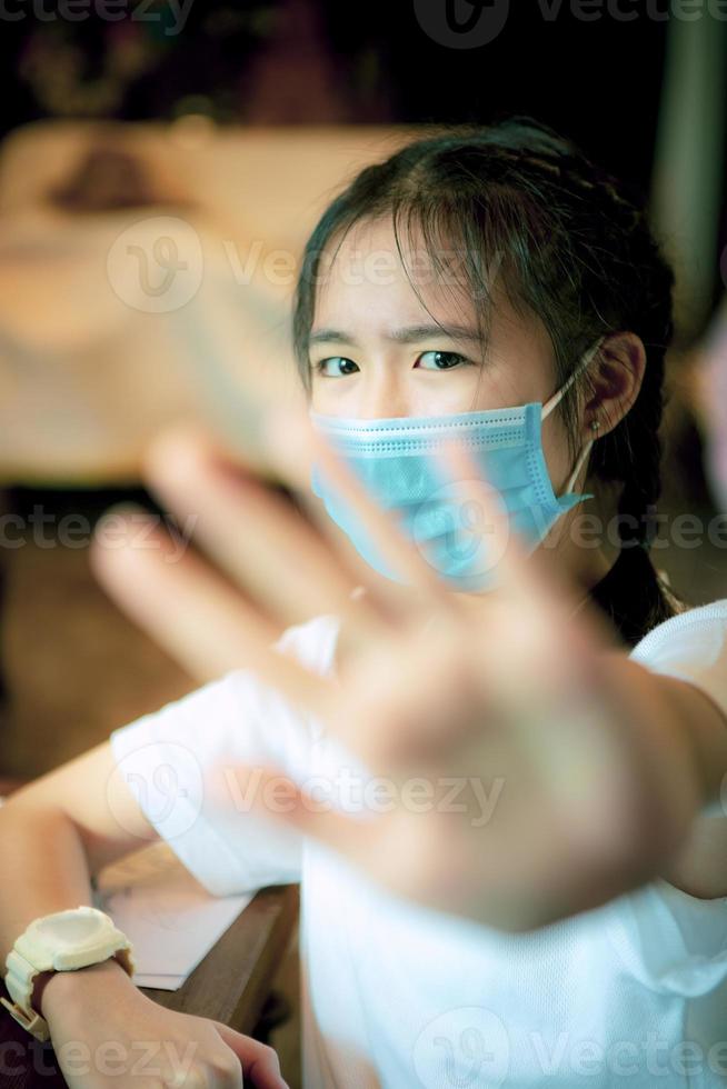 adolescente asiatico che indossa una maschera di protezione e alza la mano foto