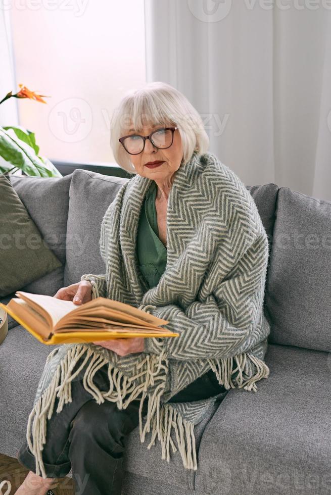 vecchia donna anziana seduta sul divano a leggere un libro a casa. educazione, maturo, concetto di svago foto