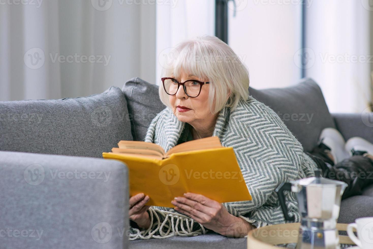 vecchia donna anziana posa sul divano a leggere un libro. educazione, maturo, concetto di svago foto