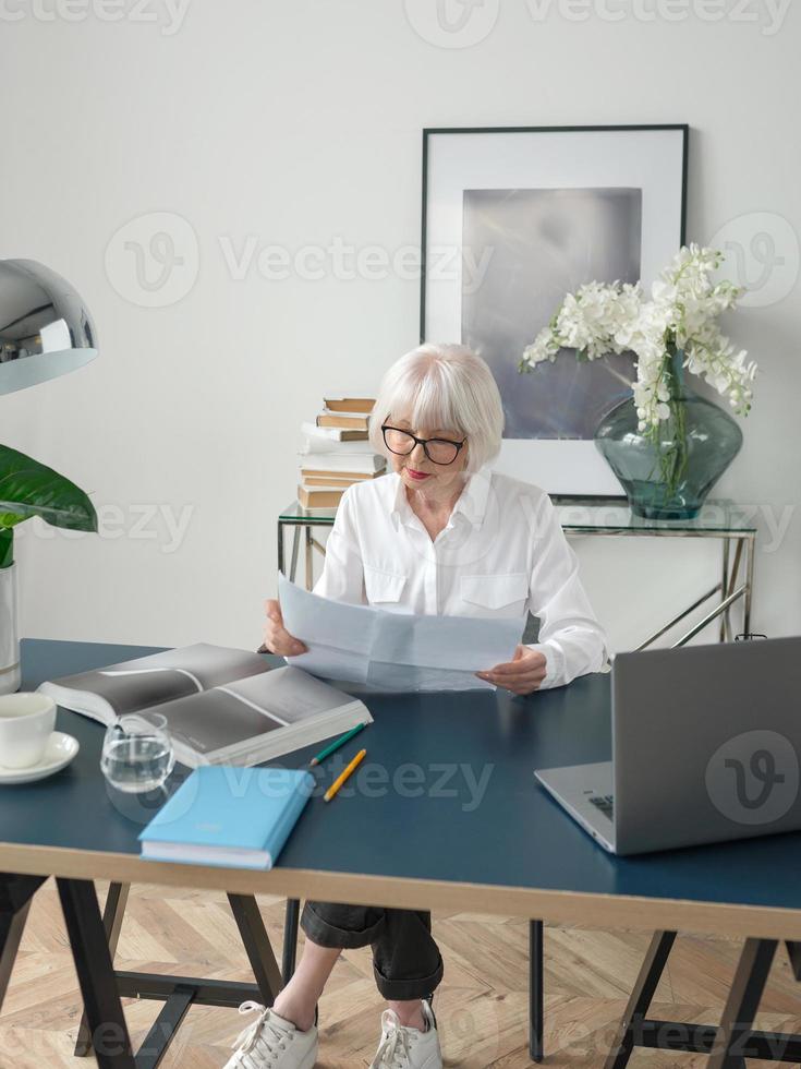 donna anziana bella capelli grigi in camicetta bianca felice in ufficio. lavoro, persone anziane, problemi, successo, trovare una soluzione, sperimentare il concetto foto