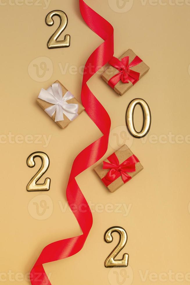 nuovo anno 2022. vista dall'alto mockup di capodanno su sfondo beige nastro rosso, confezione regalo, numeri d'oro e scintillii multicolori. impaginazione di cartoline, inviti. foto
