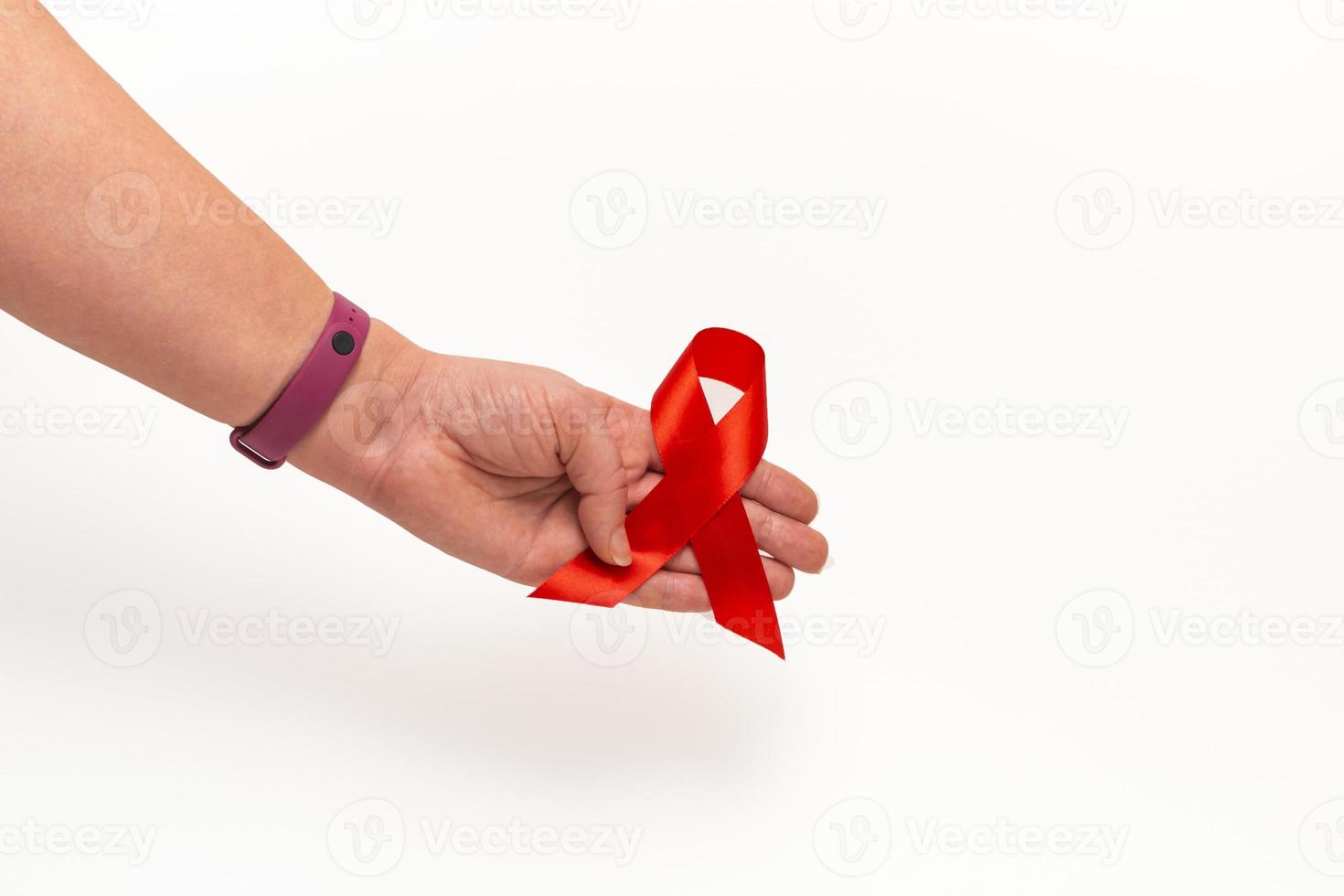 concetto medico per la giornata mondiale dell'AIDS a dicembre. il rosso aiuta il nastro di consapevolezza stretto nella mano di una donna su uno sfondo bianco. avvicinamento foto