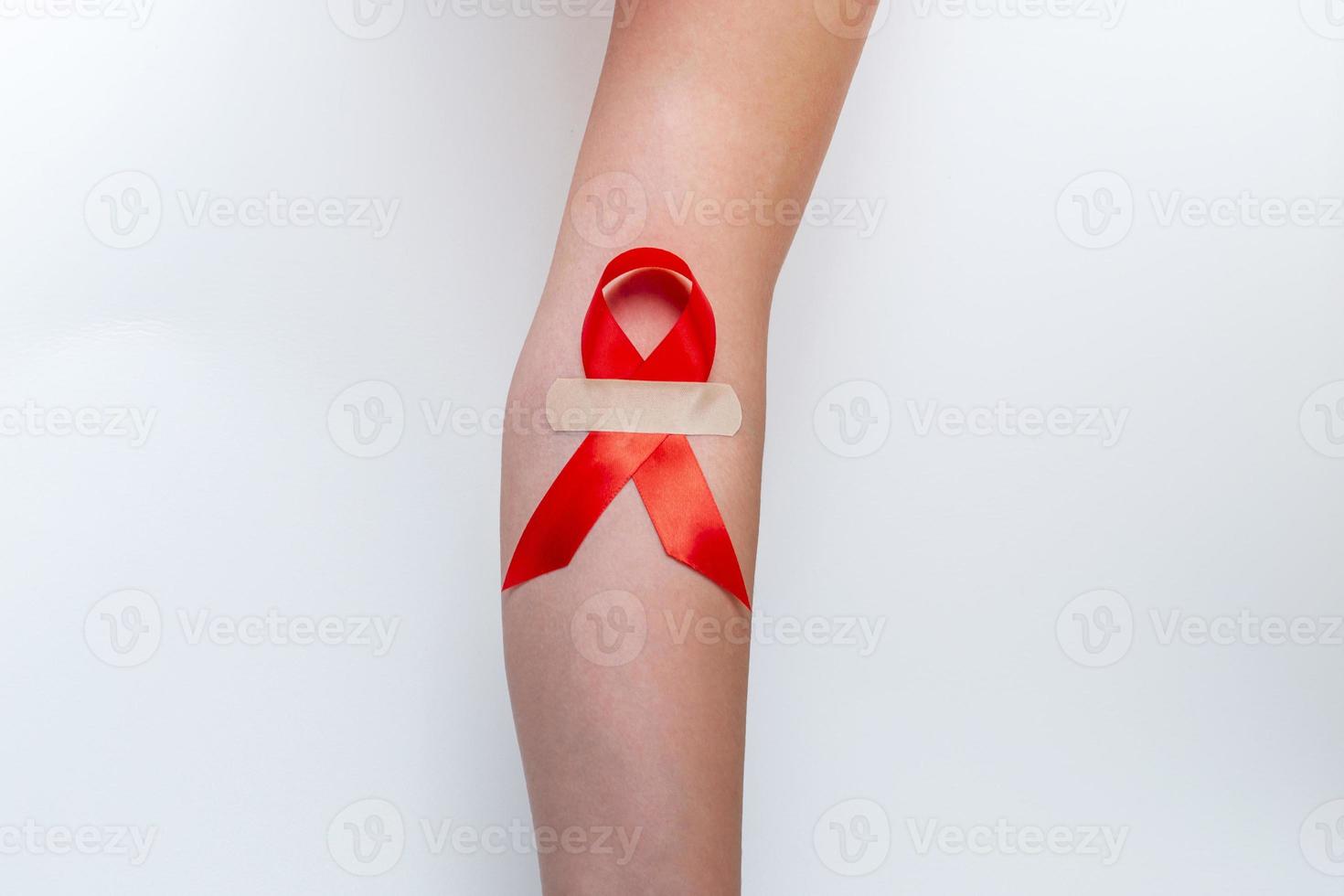 concetto medico per la giornata mondiale dell'AIDS a dicembre. il rosso aiuta il nastro di consapevolezza stretto nella mano di una donna su uno sfondo bianco. avvicinamento foto