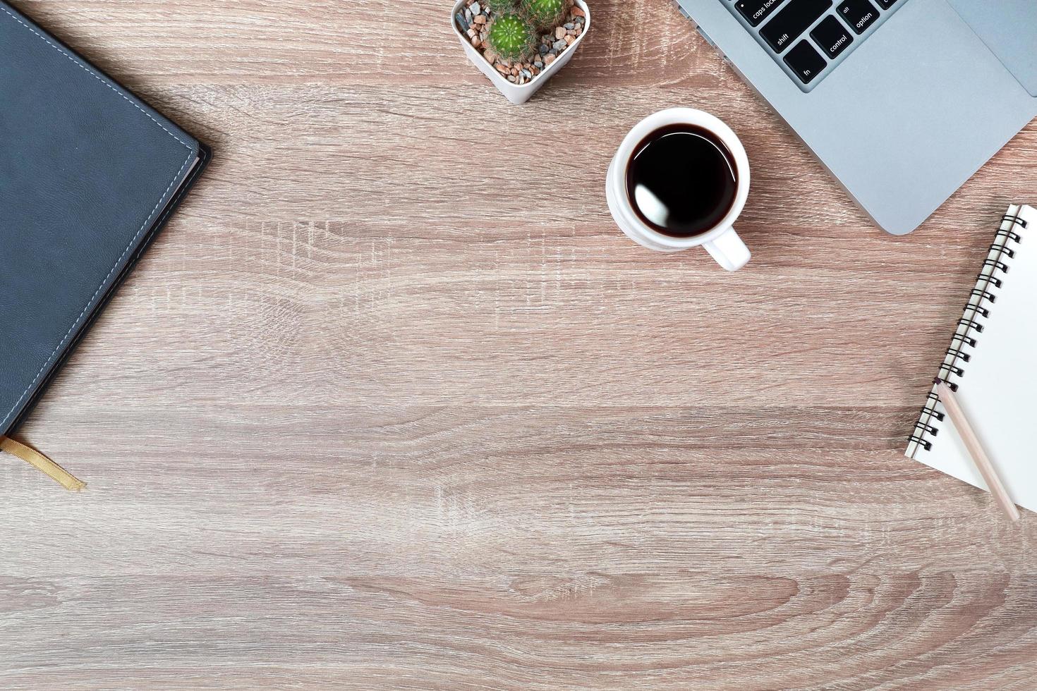 tavolo in legno da lavoro tecnologico con computer portatile, tazza da caffè e pianta foto