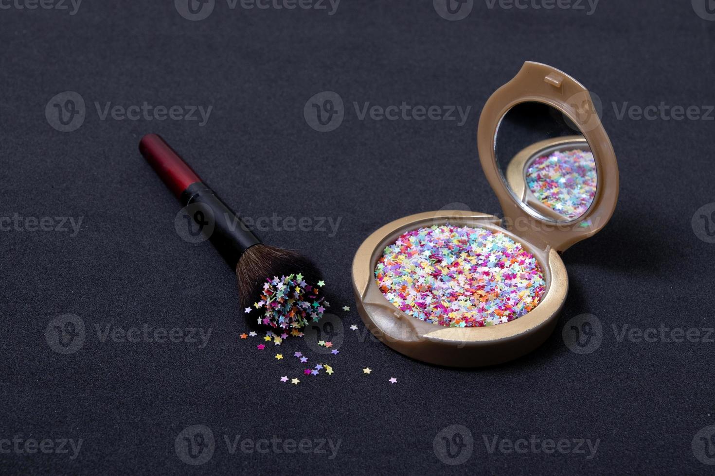 polvere per il trucco e pennello cosmetico con stelle glitterate su sfondo nero foto