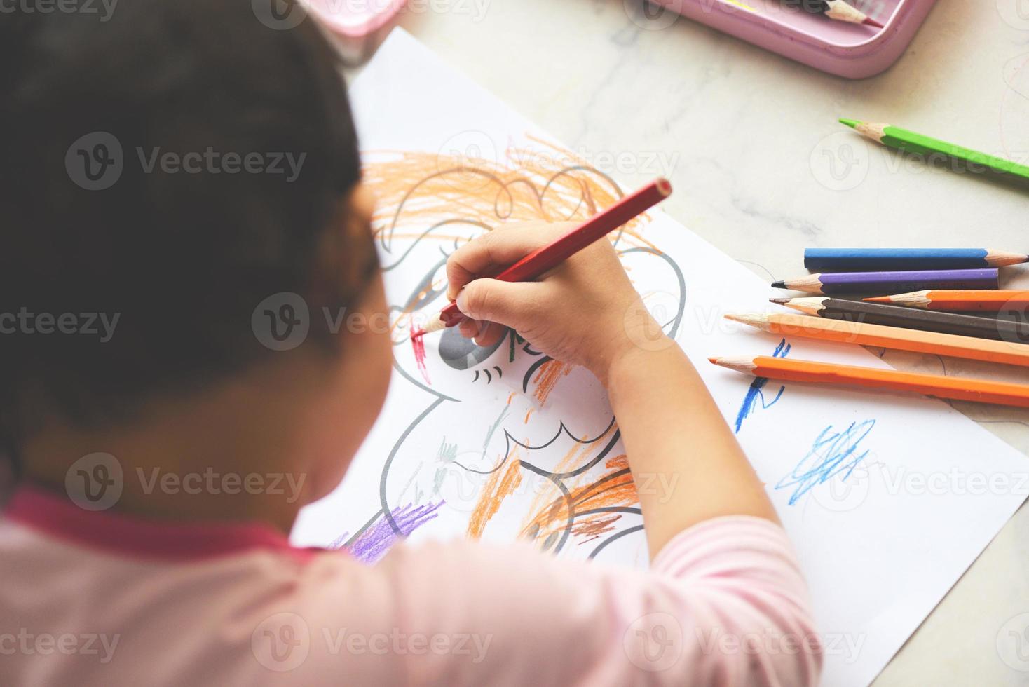 bambina che dipinge su un foglio di carta con matite colorate sul tavolo di legno a casa - impara il bambino a disegnare immagini e pastelli colorati foto