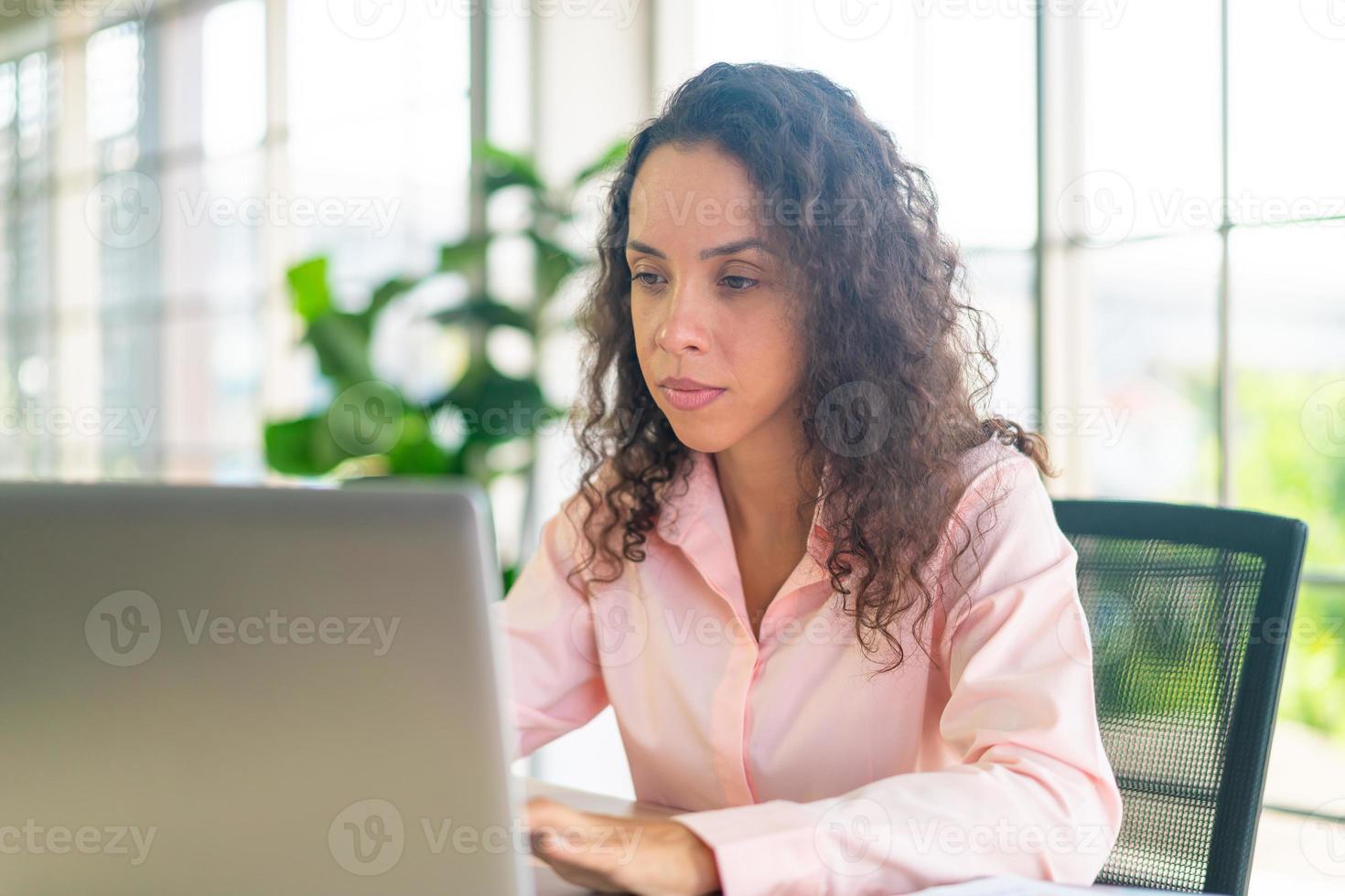 donna latina che lavora con laptop e carta sullo spazio di lavoro foto