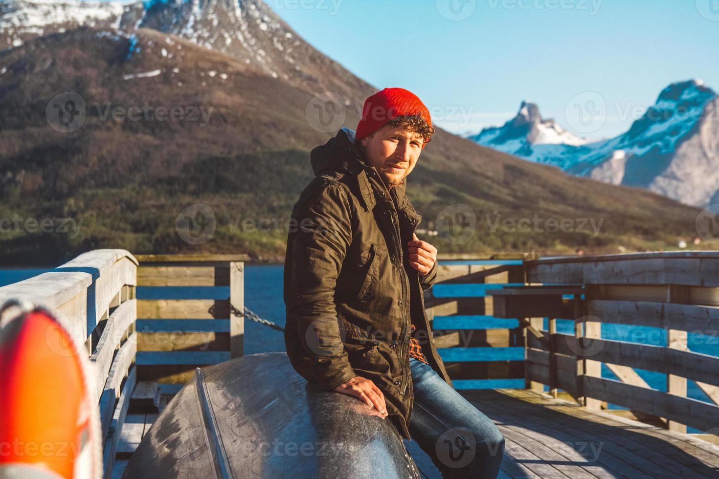 l'uomo viaggiatore si siede su una barca vicino a un molo di legno sullo sfondo di un lago di montagna foto