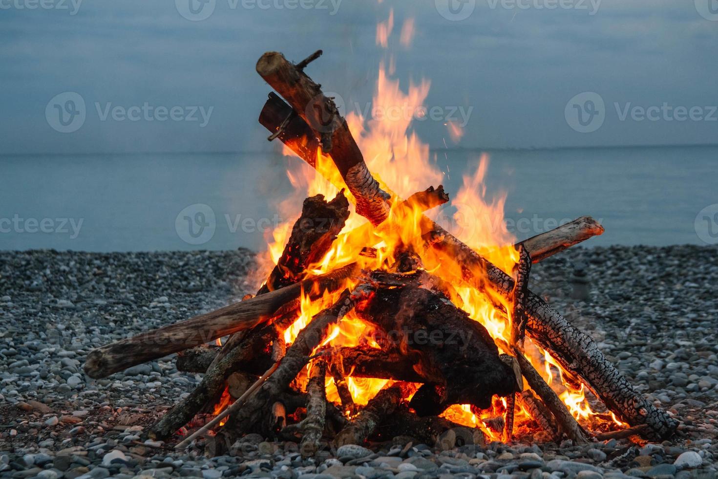 un falò sulla spiaggia. un falò su una spiaggia di pietra. fuoco sulla spiaggia - messa a fuoco selettiva, copia dello spazio. fuoco solitario in riva al mare foto