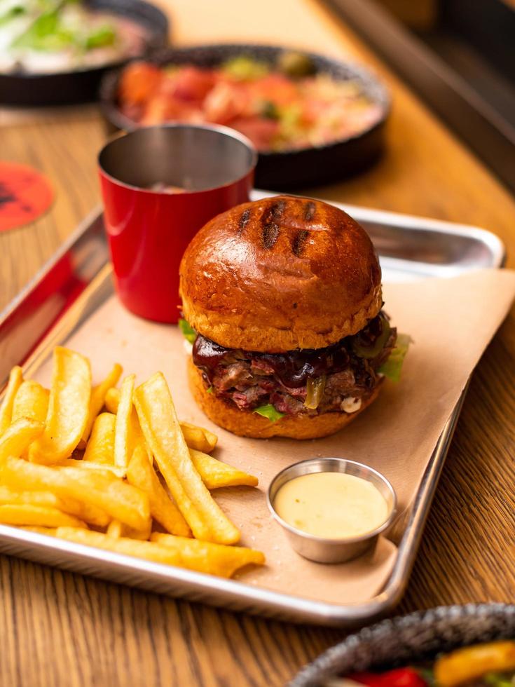 gustoso hamburger alla griglia con manzo, formaggio, pancetta e salsa su un tavolo di legno con patatine fritte e birra foto