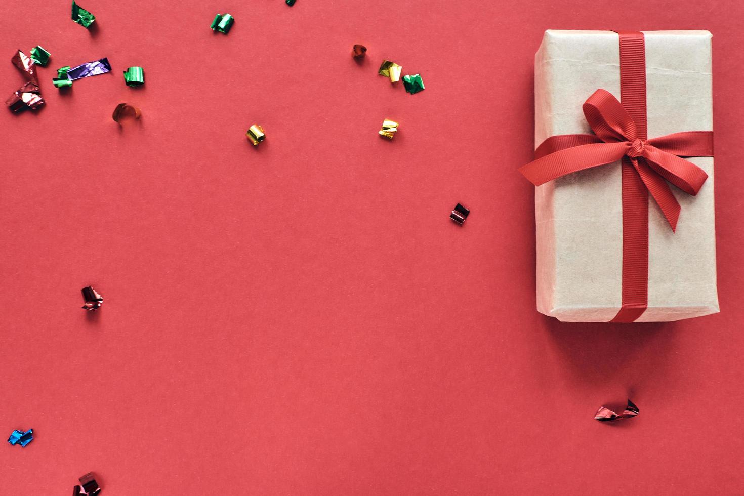 composizione di natale. confezione regalo con nastro rosso e decorazioni di coriandoli su sfondo colorato di carta pastello. natale, inverno, concetto di celebrazione del nuovo anno. disposizione piatta, vista dall'alto, copia spazio foto