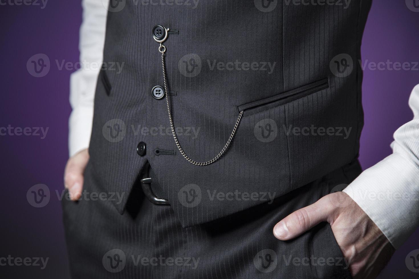 uomo in abiti classici con orologio da tasca appeso al gilet e mani nelle tasche foto