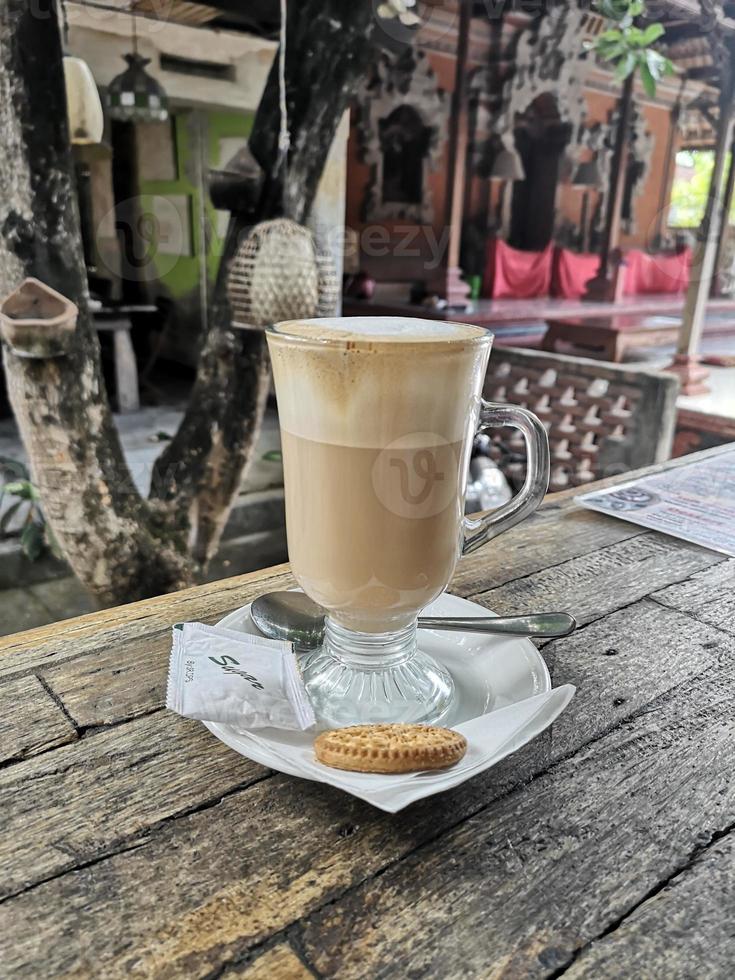 caffè latte in un bicchiere lungo con un biscotto su un tavolo di legno foto