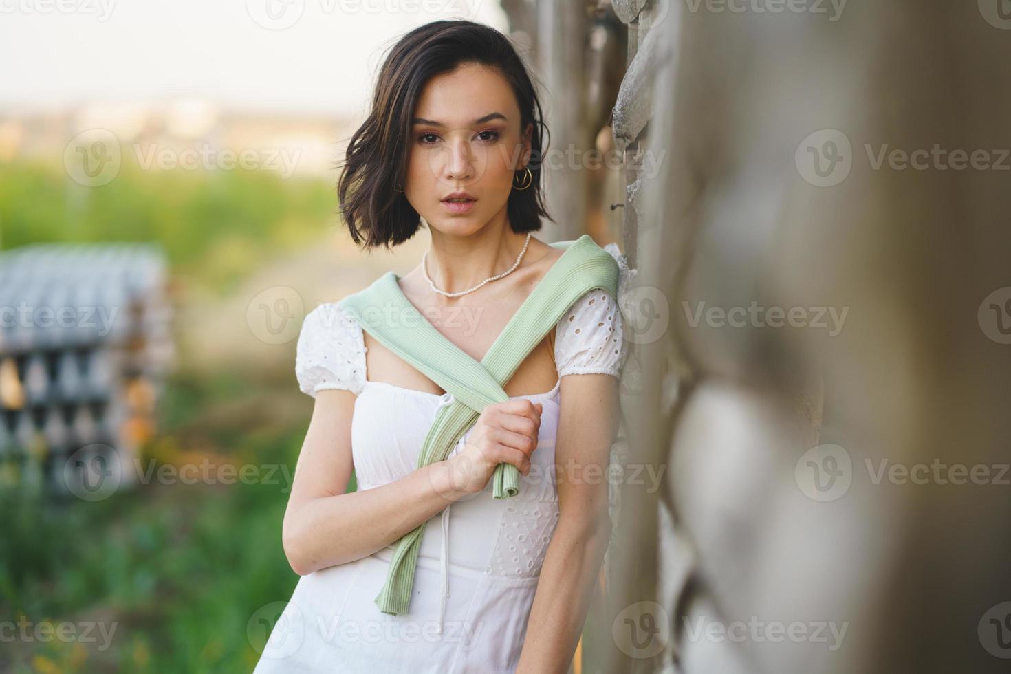 donna asiatica, in posa vicino a un capannone per l'essiccazione del tabacco, che indossa un abito bianco e stivali di gomma verdi. foto