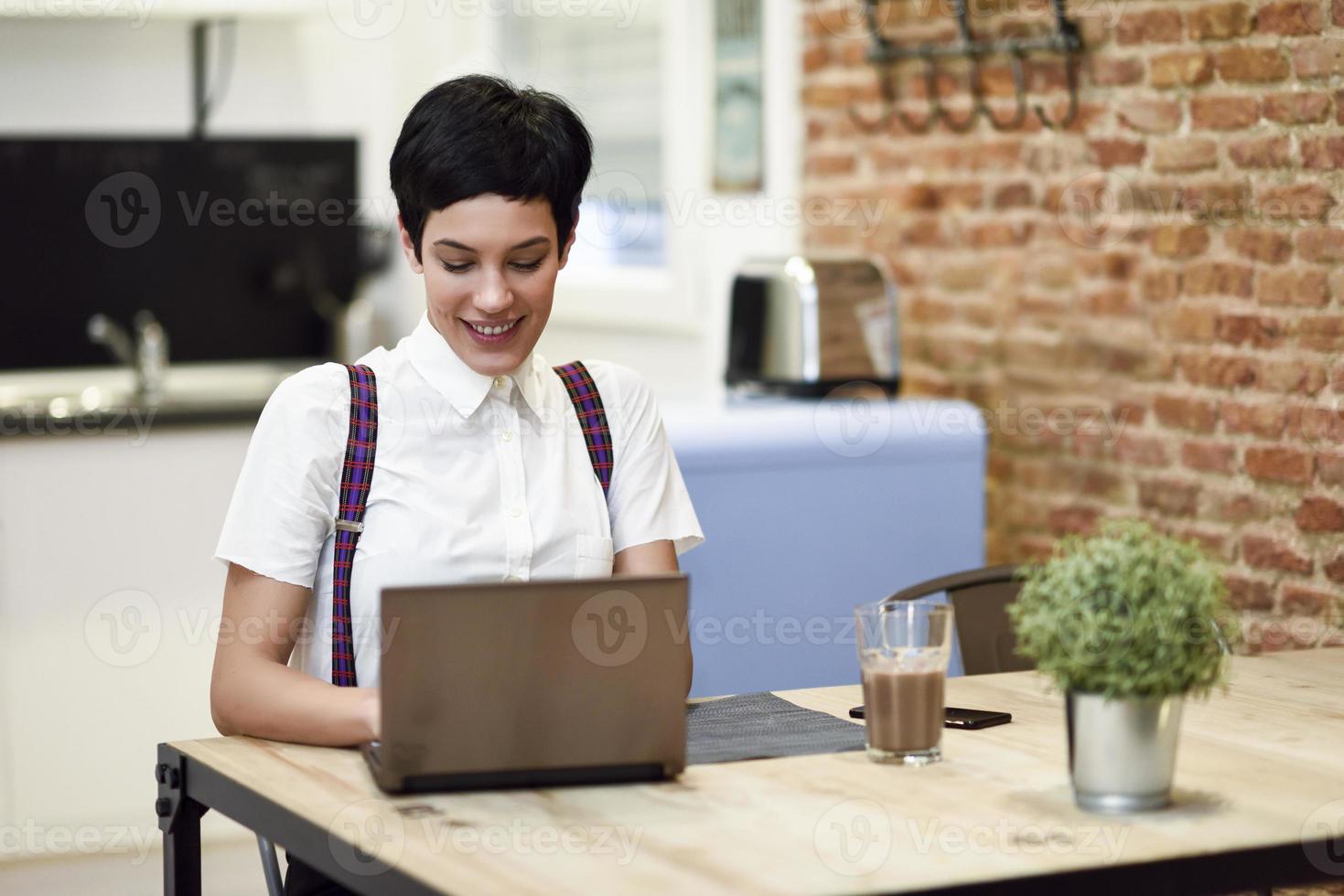 giovane donna con taglio di capelli molto corto digitando con un computer portatile a casa. foto