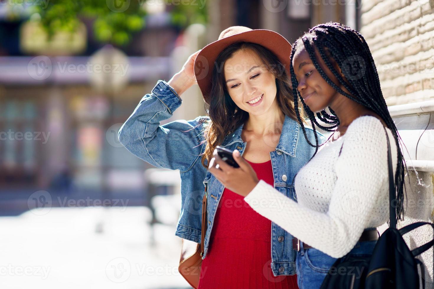 due amici che guardano insieme il loro smartphone. donne multietniche. foto