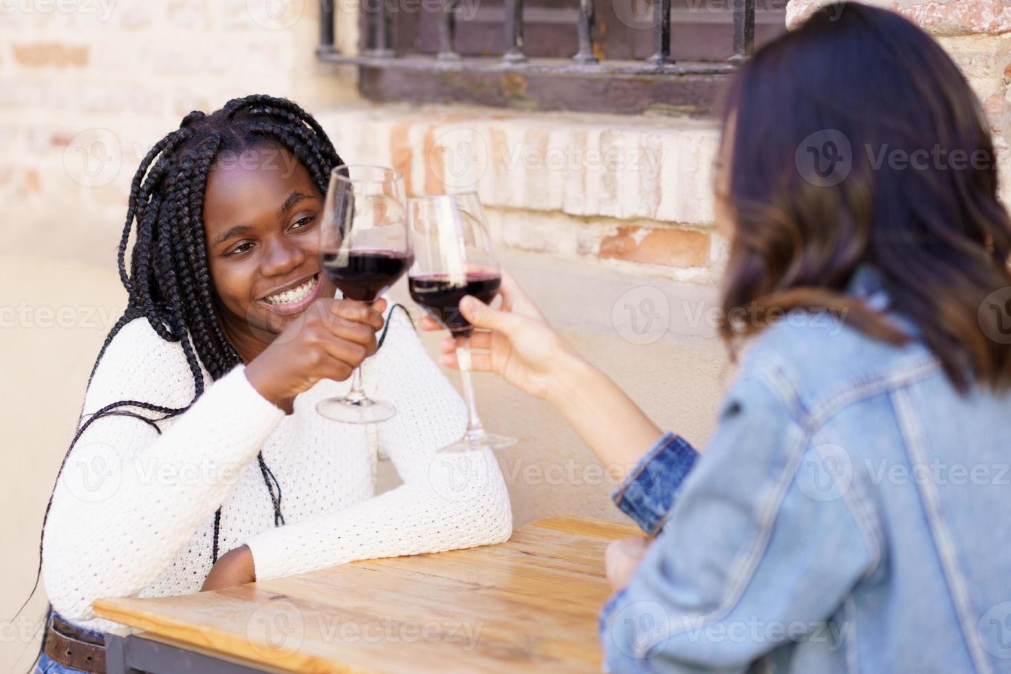 due donne che fanno un brindisi con vino rosso sedute a un tavolo fuori da un bar. foto